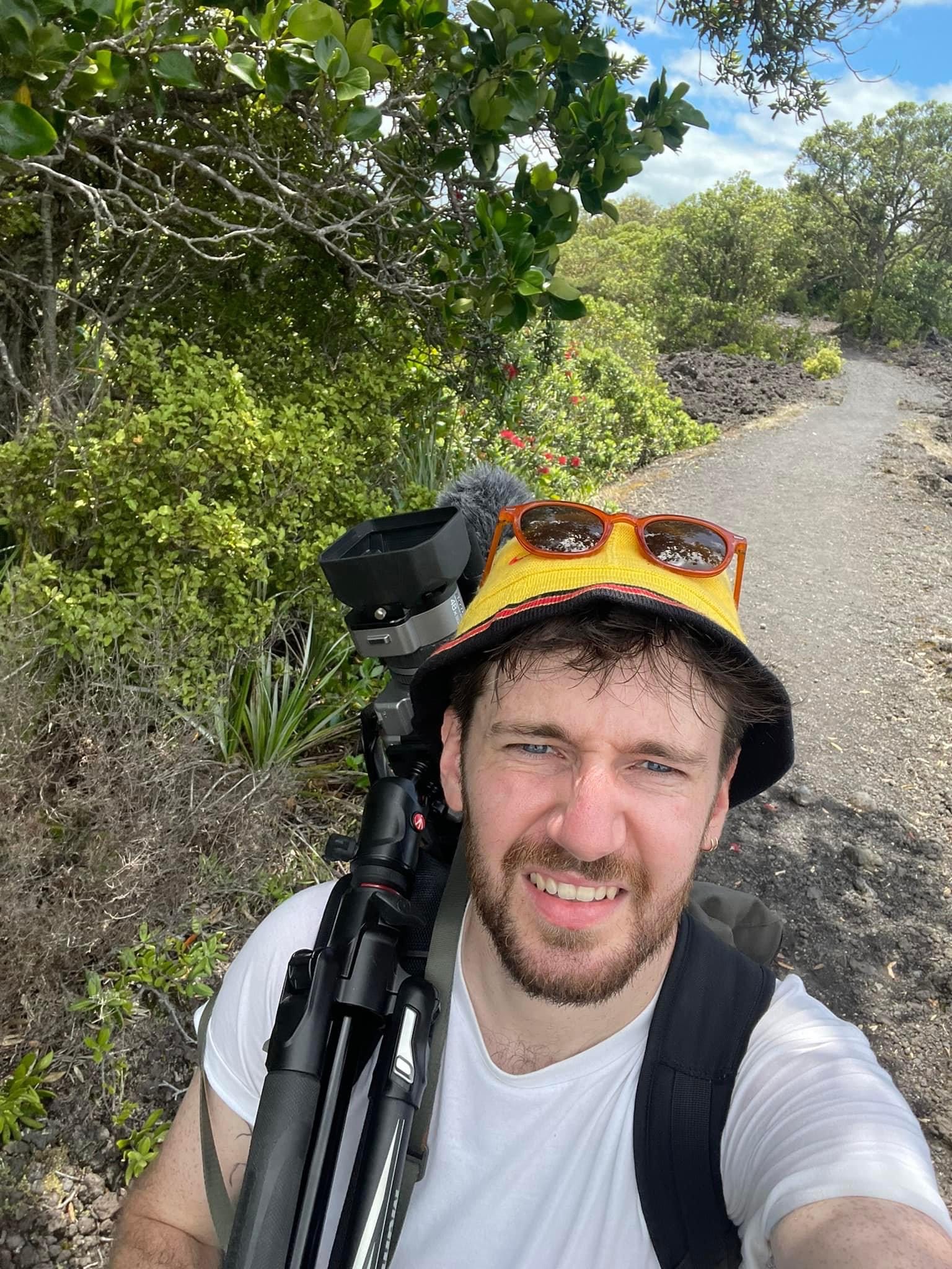 image of man wearing hat and carrying camera on a trail outdoors