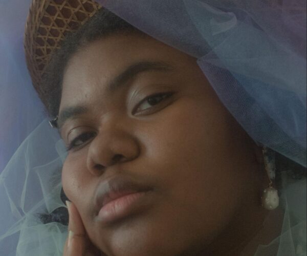 Headshot of woman with dark skin wearing a hat